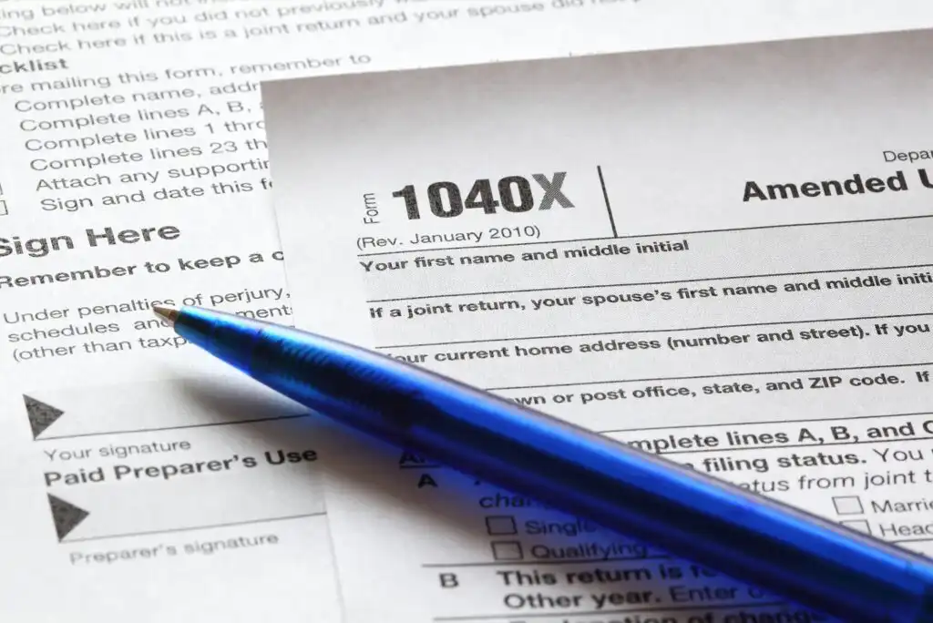 A close-up of a blue pen resting on an IRS Form 1040X, an amended U.S. individual tax return, with other tax documents partially visible underneath.