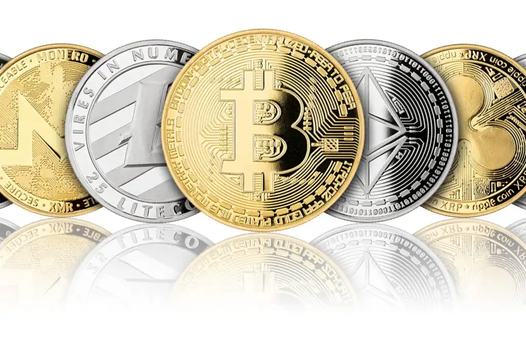Five physical coins representing cryptocurrencies—Monero, Litecoin, Bitcoin, Ethereum, and Ripple—are arranged in a row, showing their distinctive logos and designs with a reflection below.