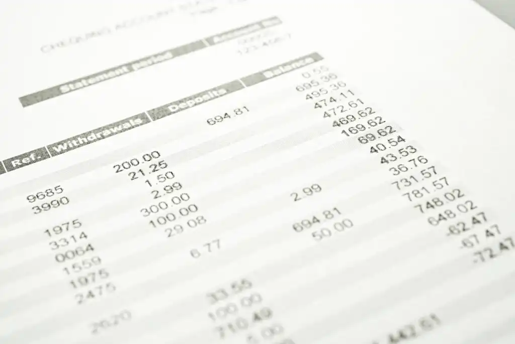 A close-up of a printed bank statement showing transaction details, including dates, reference numbers, withdrawals, deposits, and balances in a financial account. The text is slightly out of focus.
