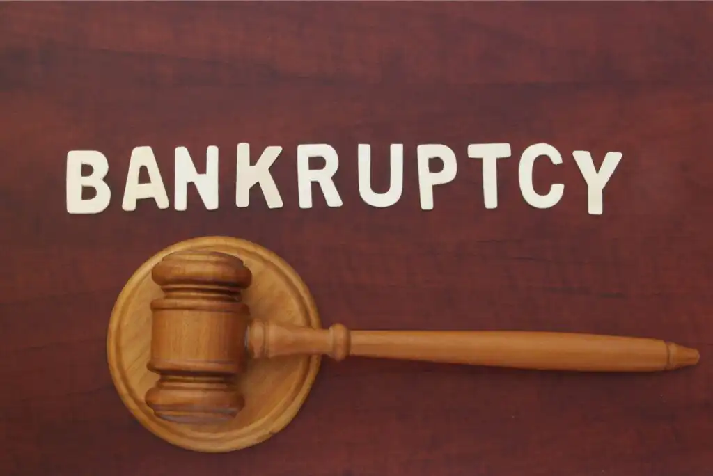 A wooden judge’s gavel rests on a desk beneath the word BANKRUPTCY spelled out in white letters.