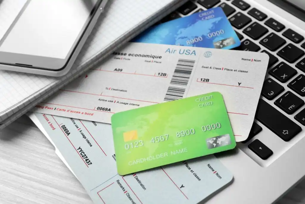 Several airline boarding passes and credit cards are scattered on a laptop keyboard, with a smartphone and notepad nearby, suggesting online travel booking or planning.