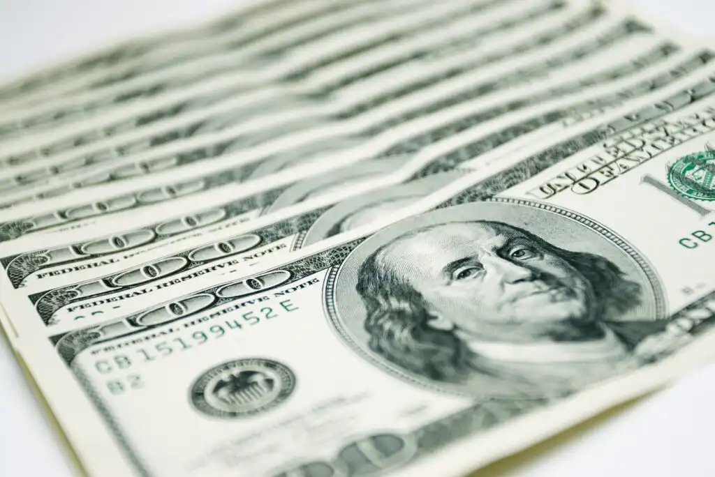A close-up view of several overlapping U.S. one hundred dollar bills, featuring the portrait of Benjamin Franklin.