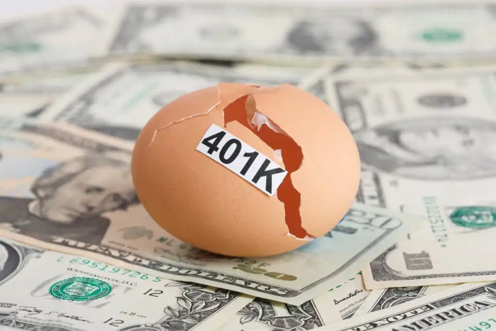 A cracked egg labeled 401K sits on a pile of U.S. dollar bills, symbolizing a broken or depleted retirement fund.