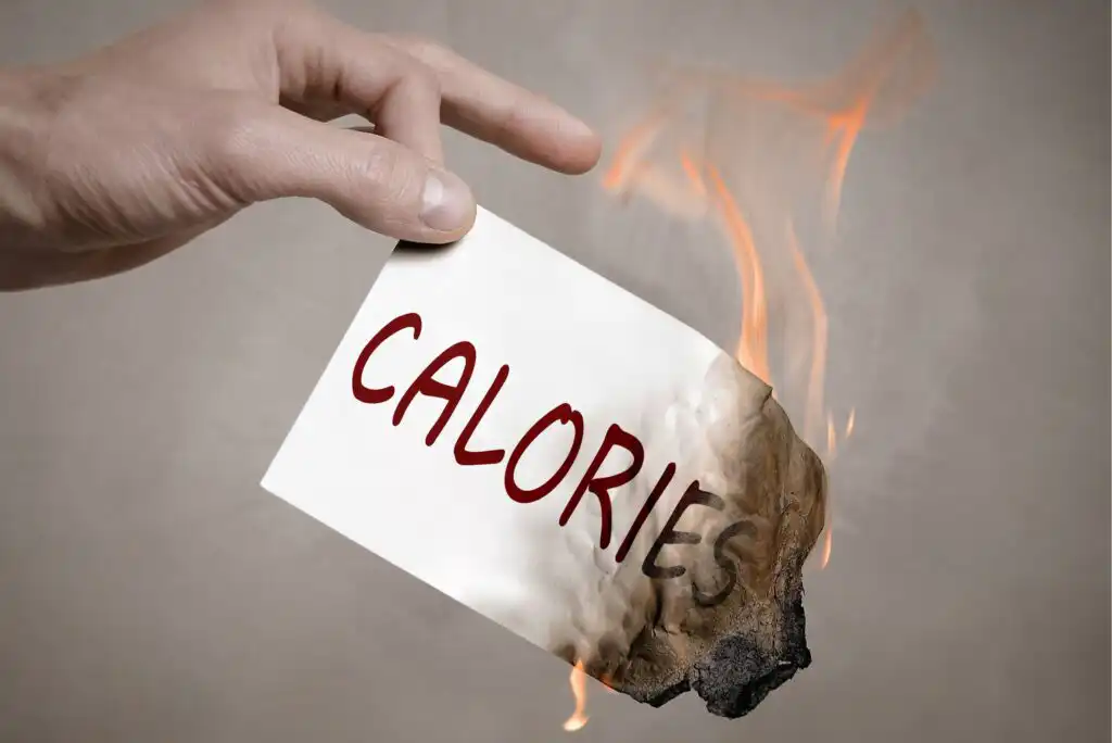 A hand holds a white card with the word CALORIES written on it in red; the edge of the card is burning with visible flames and scorch marks.