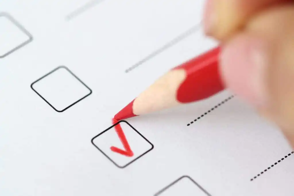 A close-up of a red pencil marking a check in a checkbox on a paper form, with other empty checkboxes and dotted lines visible.