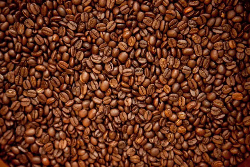 A close-up view of a large pile of roasted coffee beans, showing their glossy, brown surfaces and varied shapes.