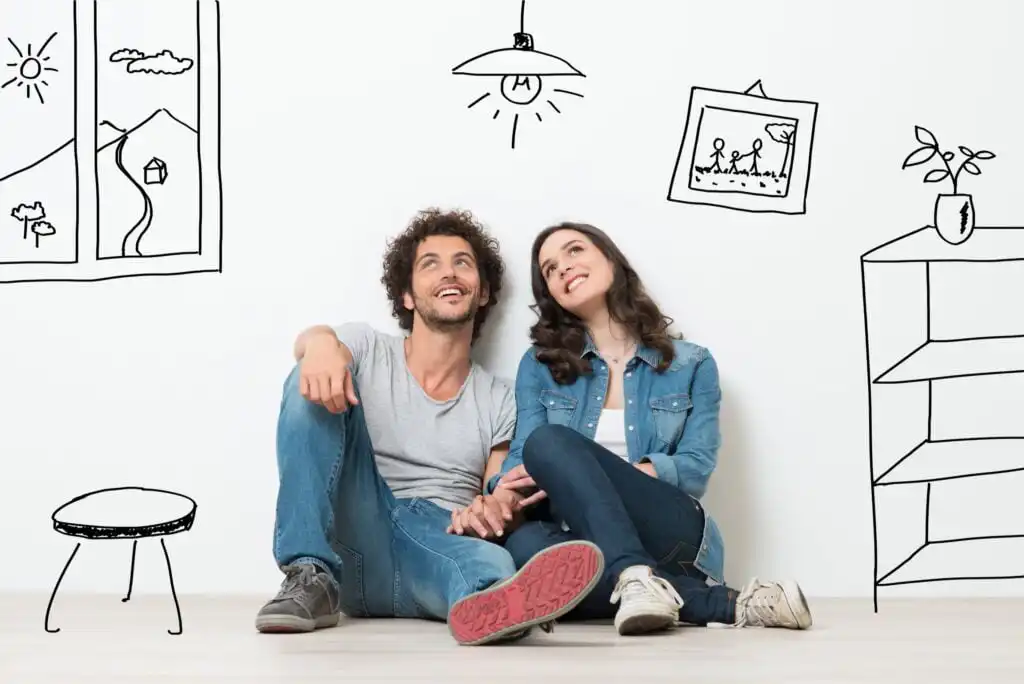 A smiling couple sits on the floor against a white wall, holding hands. Around them, playful black line drawings depict furniture, a window, a plant, a lamp, and a family photo frame.