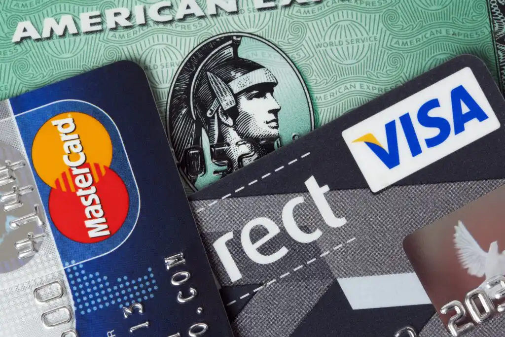 A close-up photo of several credit cards, including MasterCard, Visa, and American Express, arranged in an overlapping stack. The cards display their logos and partial card information.