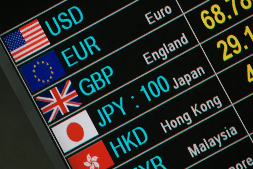 A digital currency exchange rate board displays flags, currency codes (USD, EUR, GBP, JPY, HKD), and names of their corresponding countries or regions, including the US, EU, England, Japan, and Hong Kong.