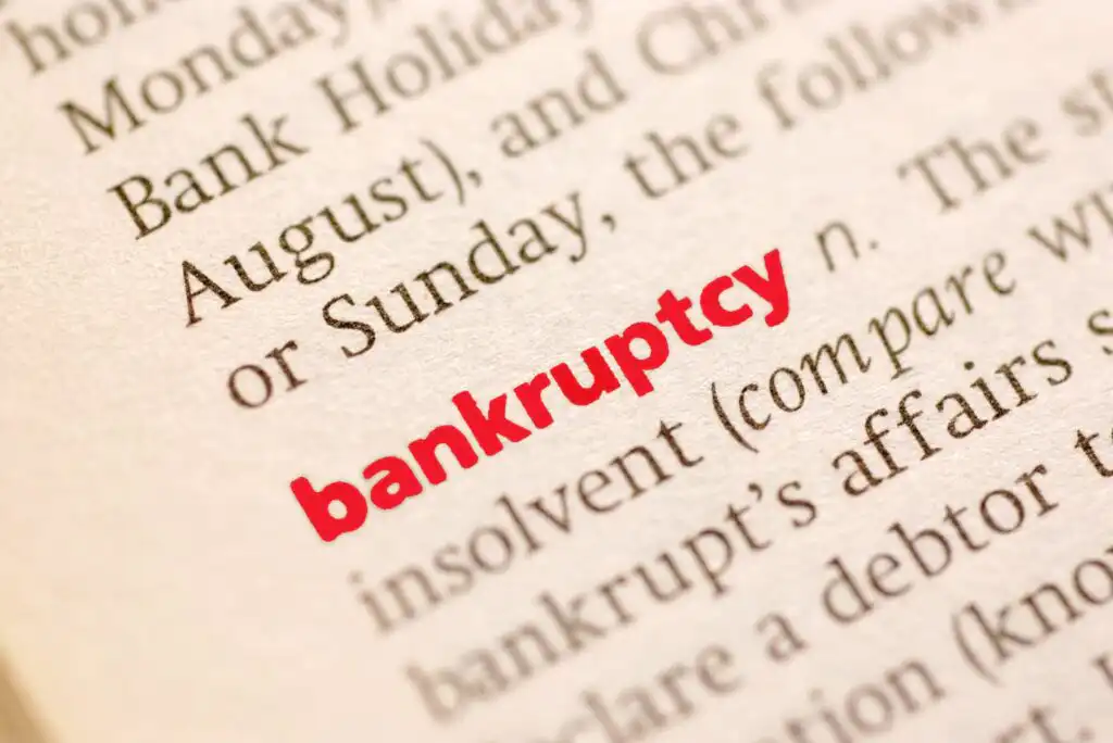 A close-up of a dictionary page with the word bankruptcy highlighted in bold red text among surrounding definitions and words in black print.