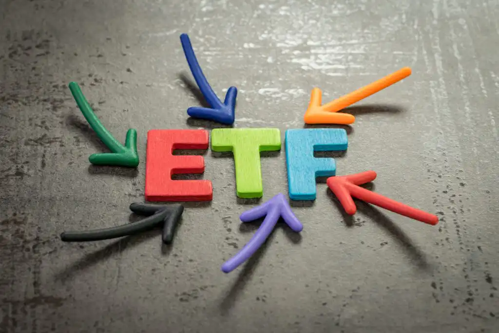 Colorful wooden letters spelling ETF with eight multicolored arrows pointing toward the letters, all on a textured gray surface.