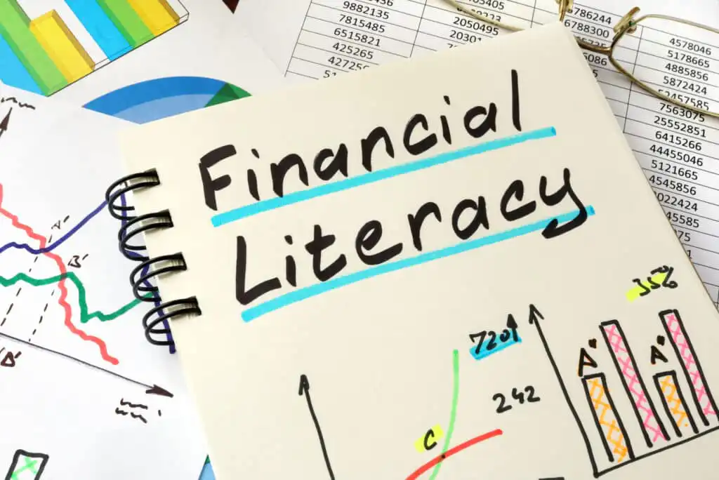 A notebook with Financial Literacy written on the cover in bold letters, surrounded by colorful charts, graphs, and spreadsheets displaying financial data and statistics.