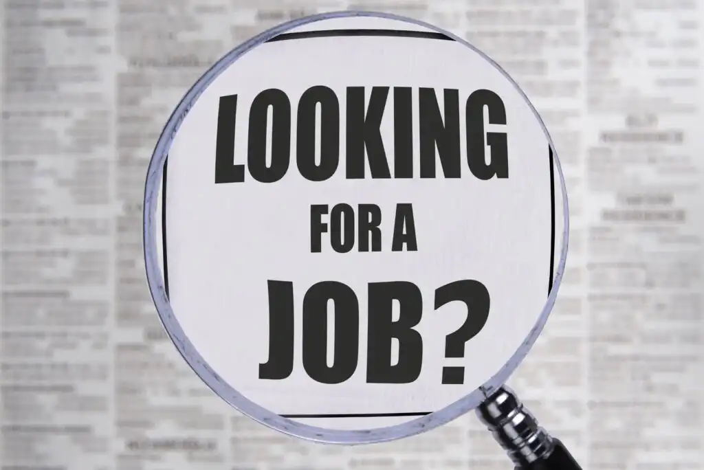 A magnifying glass focuses on the words Looking for a job? in bold black letters, with a blurred background of newspaper classified ads.