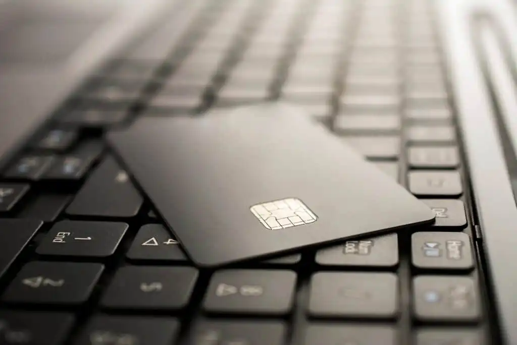 A credit card with a visible chip rests on the black keys of a laptop keyboard, suggesting online payment or internet banking.