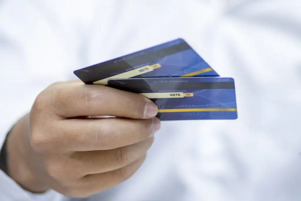 A person wearing a white shirt holds two blue credit or debit cards between their fingers, extending them forward.