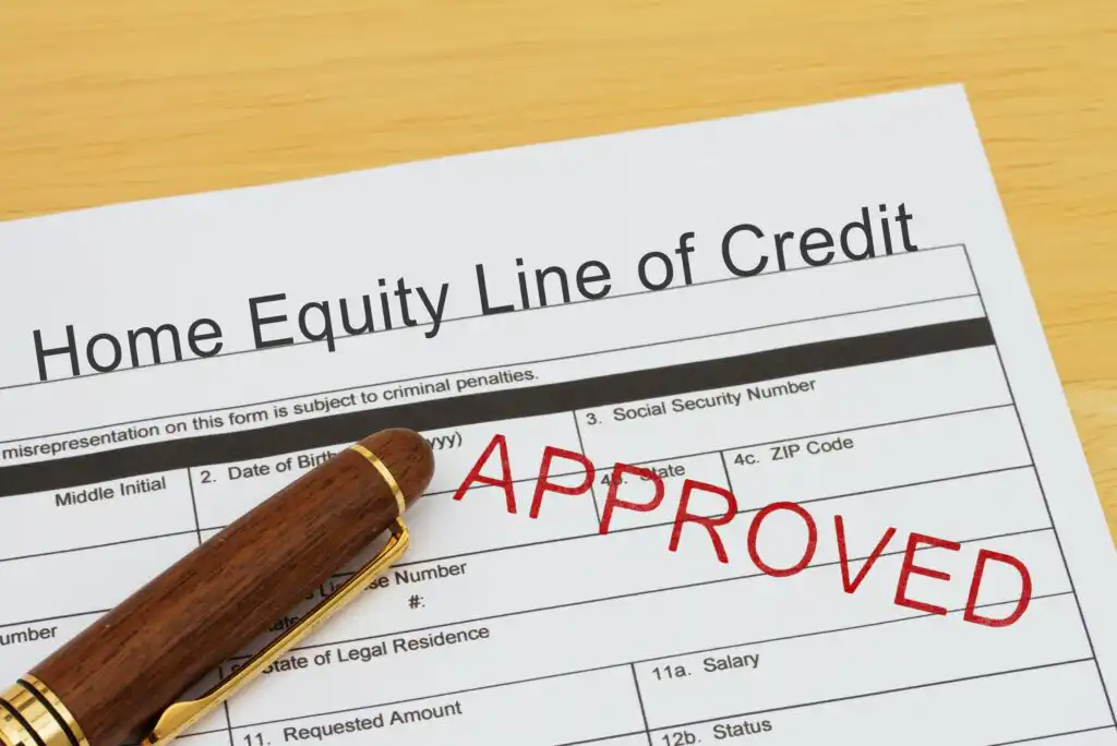 A home equity line of credit application form with a wooden pen resting on it and a large red APPROVED stamp across the paper.
