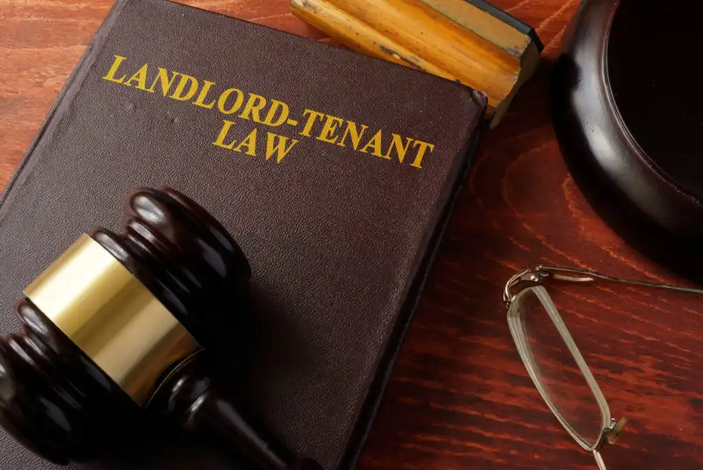 A book titled Landlord-Tenant Law is on a wooden desk, next to a judge’s gavel, a pair of eyeglasses, and part of a legal block stamp.