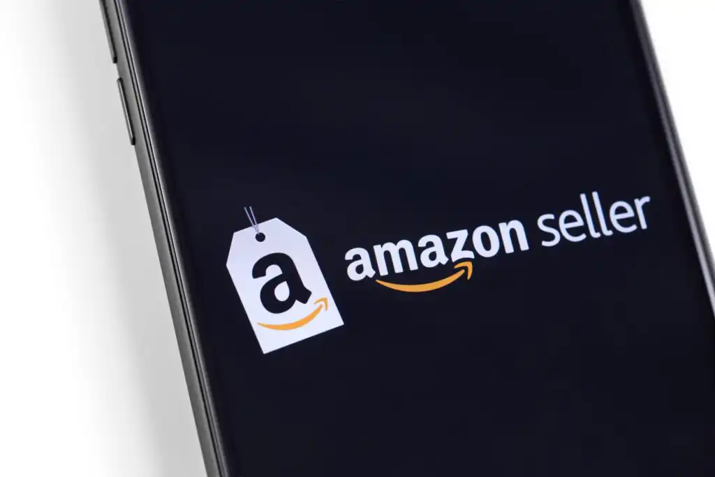 A smartphone screen displays the Amazon seller logo, featuring a price tag with the letter a and the Amazon smile arrow, on a black background.