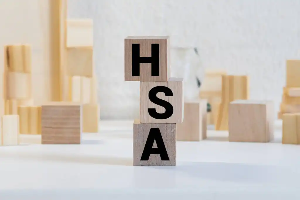 Three wooden blocks stacked vertically with large black letters H, S, and A, surrounded by other wooden blocks in the background on a white surface.