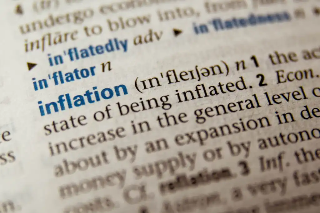 Close-up of a dictionary page showing the word inflation in bold blue letters, with its pronunciation and definition related to an increase in the general level of prices.