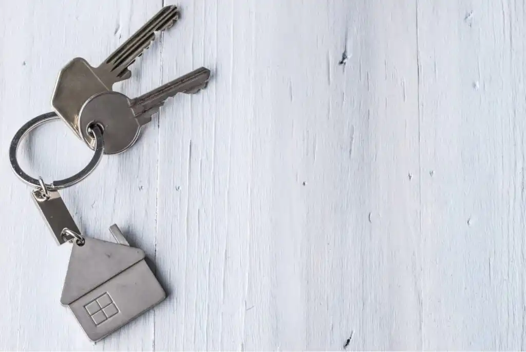 A set of two silver keys on a keyring with a house-shaped keychain, placed on a light wooden surface.