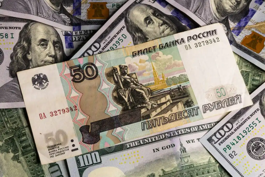 A 50 Russian ruble banknote placed on top of several overlapping 100 US dollar bills featuring Benjamin Franklin’s portrait.