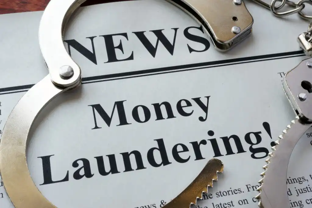 A newspaper with the headline Money Laundering! is partially covered by a pair of metal handcuffs, suggesting legal issues or crime related to financial activities.