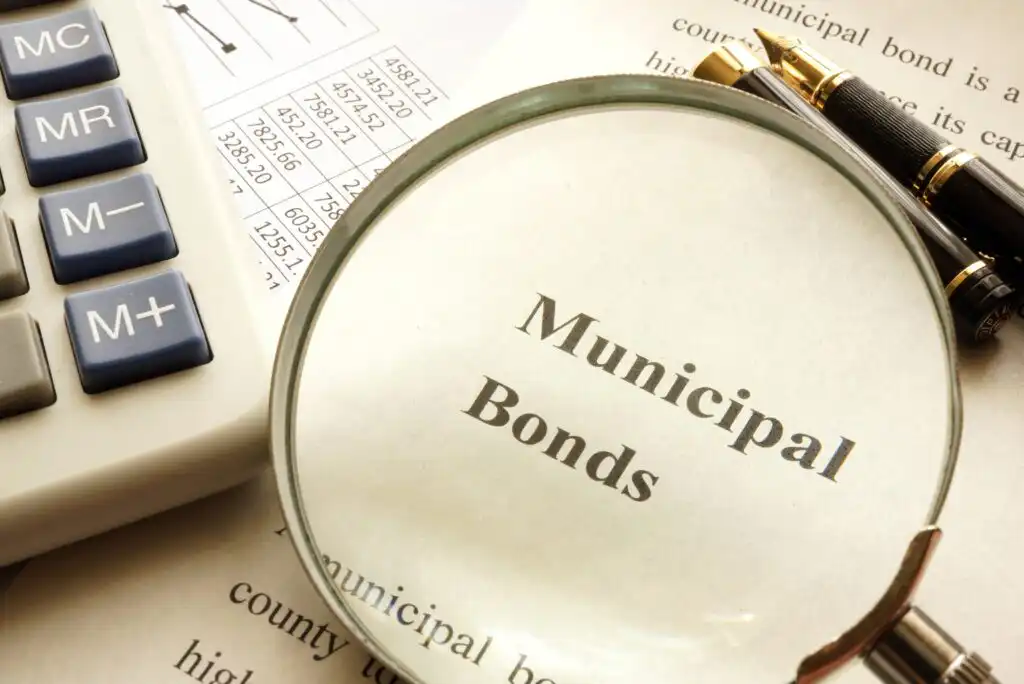 A magnifying glass highlighting the words Municipal Bonds on a document, next to a calculator, a printed table, and two pens on a desk.