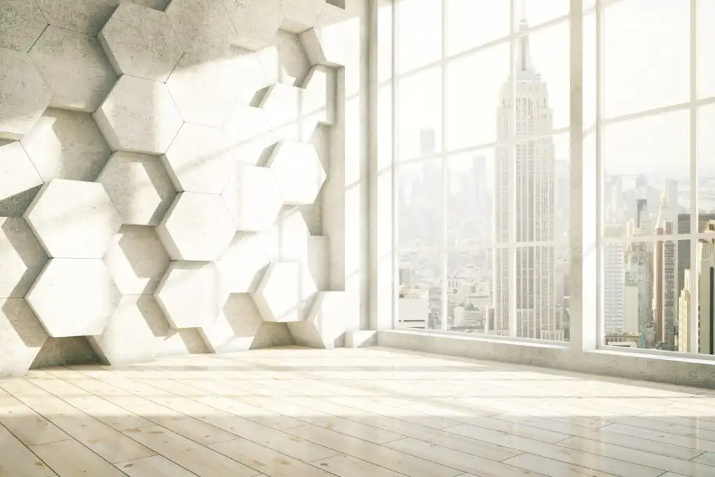A bright, modern empty room with a wooden floor, geometric hexagonal wall panels, and large windows revealing the New York City skyline with the Empire State Building in view.