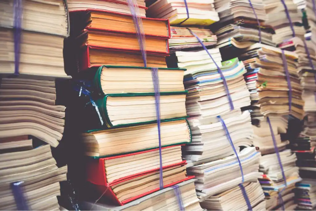 Stacks of thick books and papers bundled together with blue string, arranged closely in tall piles, creating a cluttered scene of organized reading materials.