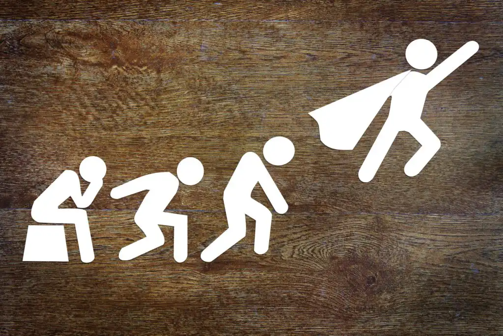 White stick figures on a wooden background show a progression: sitting, crouching, preparing to jump, and finally leaping upward with a cape, resembling a superhero.