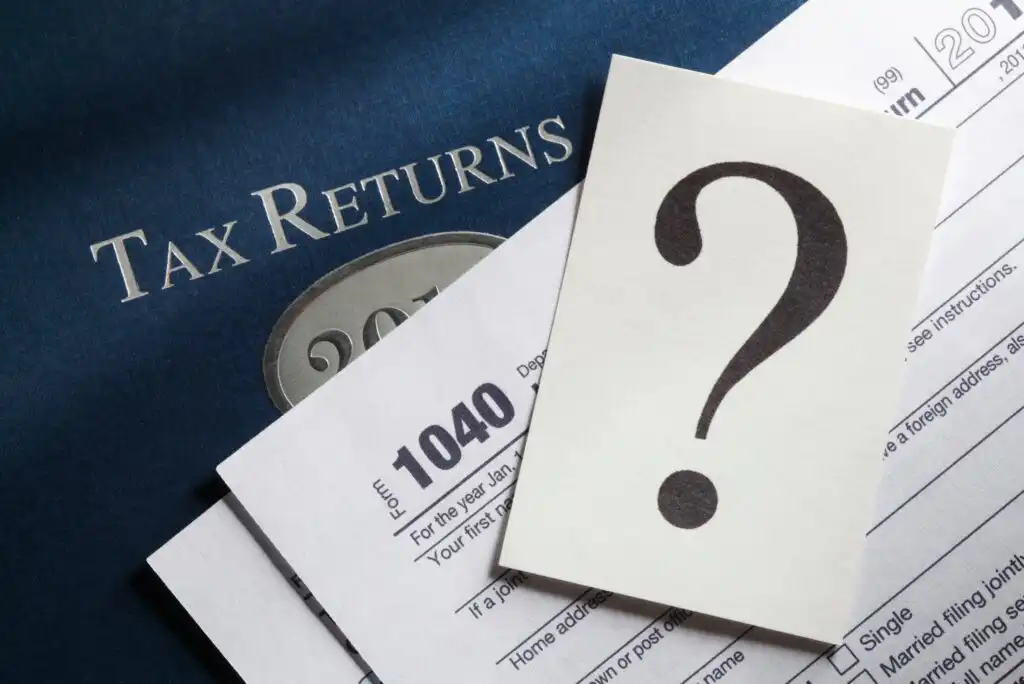 A tax return folder, 1040 form, and a paper with a large question mark symbolize uncertainty or confusion about filing taxes.