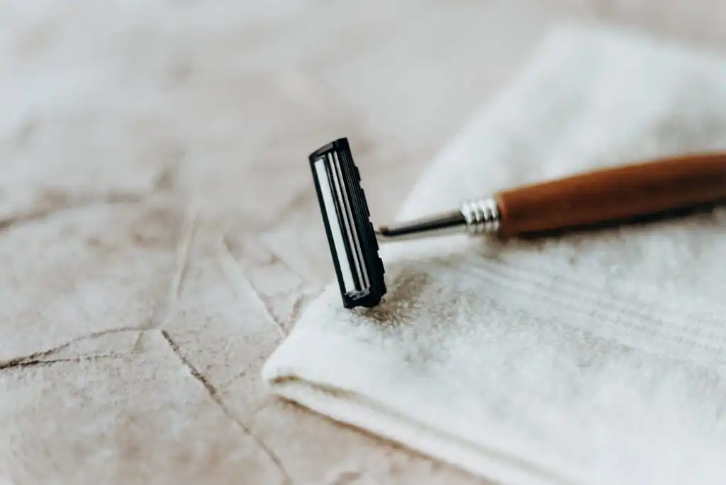 A close-up of a razor with a wooden handle resting on a white folded towel, placed on a light textured surface.