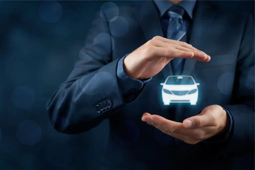 A person in a suit holds their hands around a glowing, holographic car icon, symbolizing car protection, insurance, or automotive security, with a dark, blurred background.