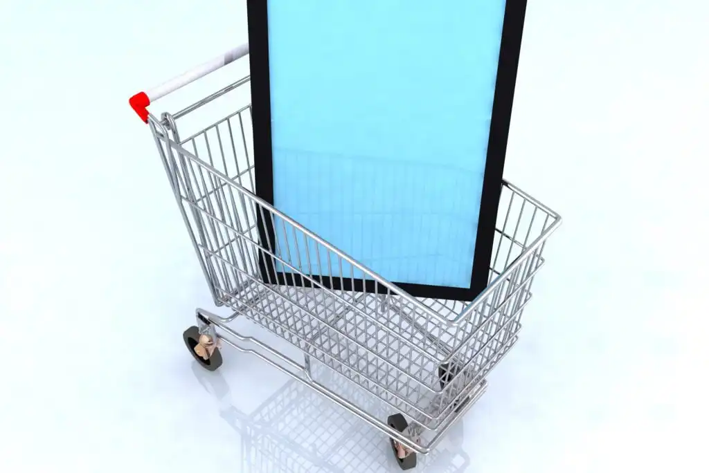 A large tablet device stands upright inside an empty shopping cart with a red handle, set against a light, plain background.