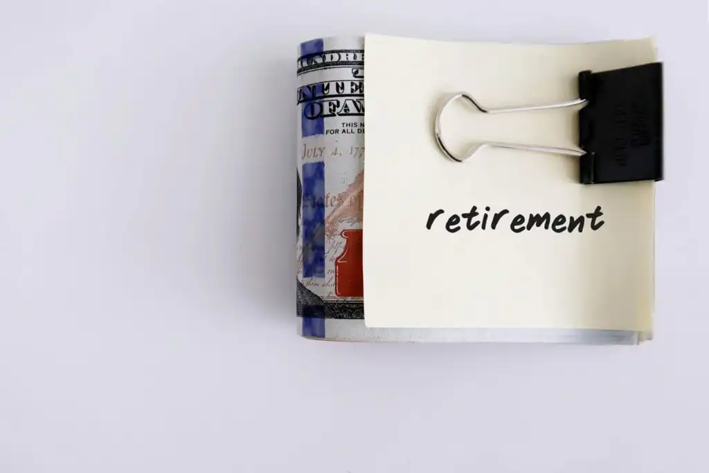 A stack of U.S. hundred-dollar bills clipped with a binder clip, with a sticky note labeled retirement placed on top, symbolizing saving money for retirement.