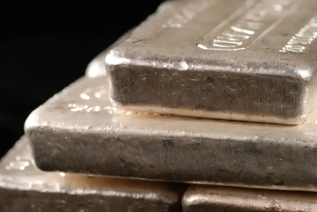 Close-up of stacked silver bars with a slightly rough texture and engraved details, set against a dark background.