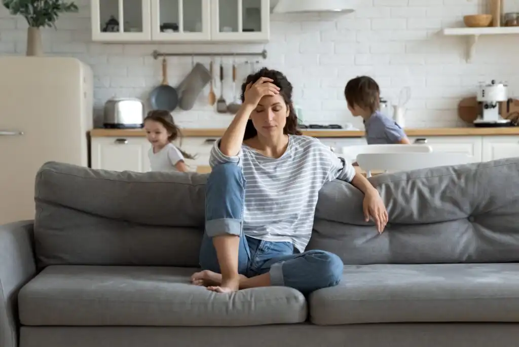 A woman sitting on a couch with her hand on her head.
