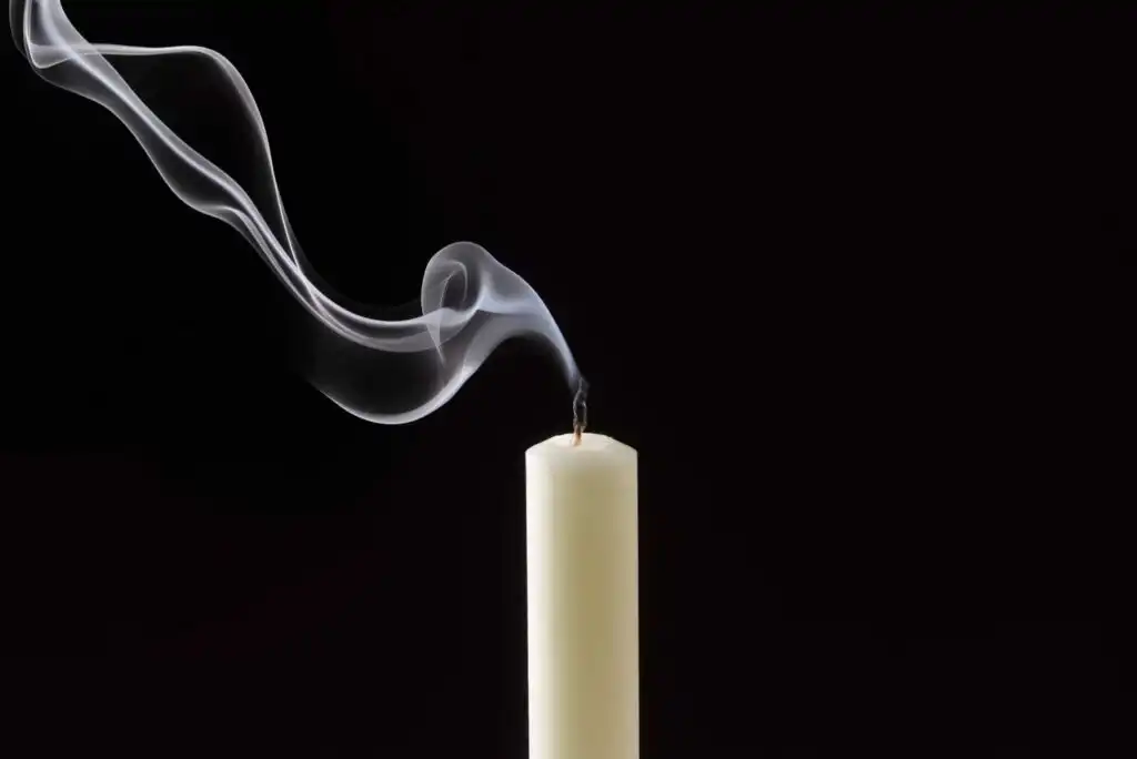 A white candle with a recently extinguished flame emits a gentle trail of smoke, curling gracefully against a black background.