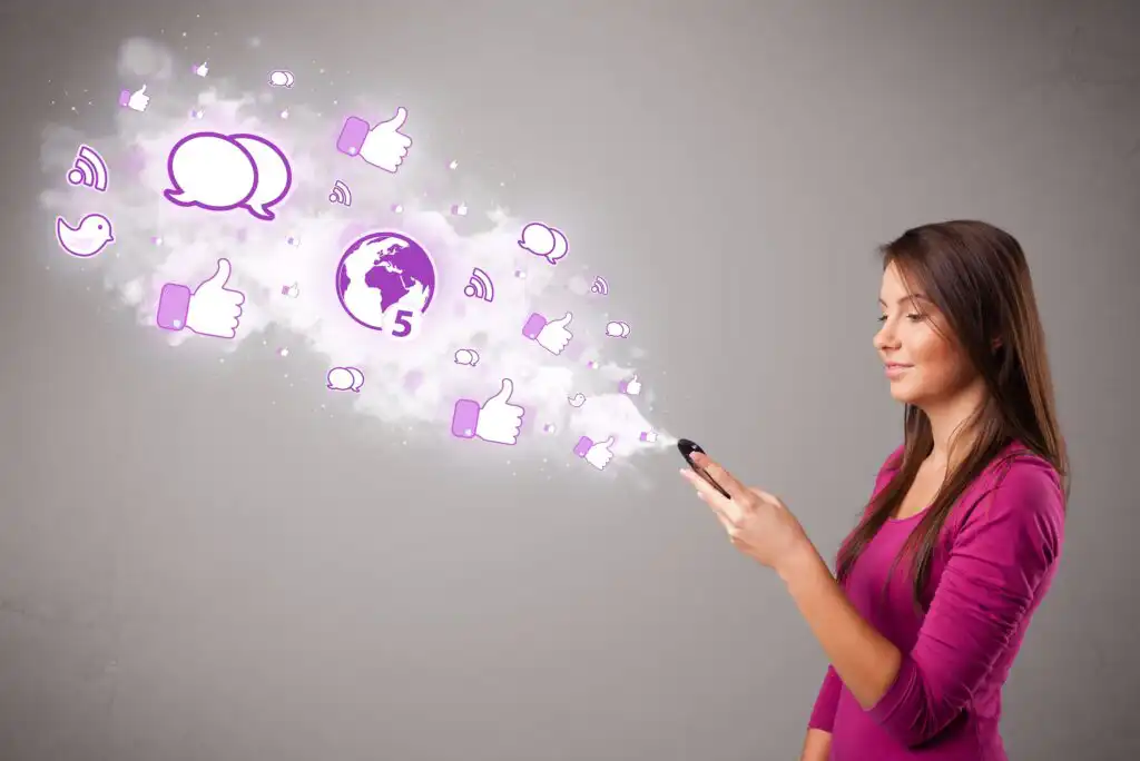 A woman in a pink shirt uses a smartphone, with glowing social media icons like thumbs up, chat bubbles, and a globe floating from the device against a gray background.