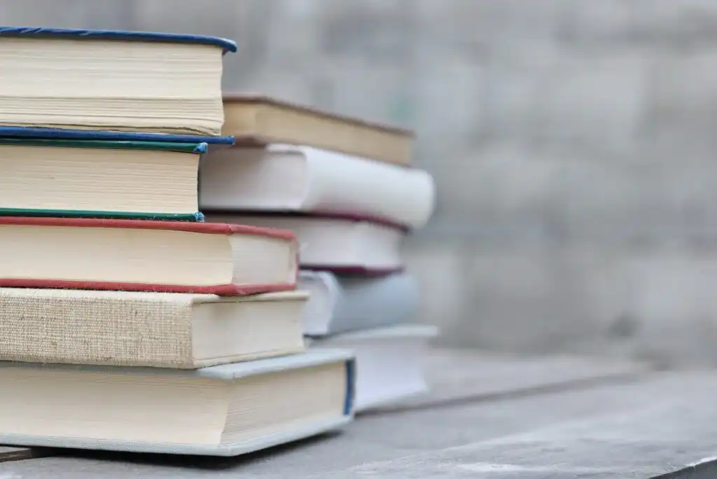 A close-up of two uneven stacks of books with various colored spines on a wooden surface, against a blurred gray background.
