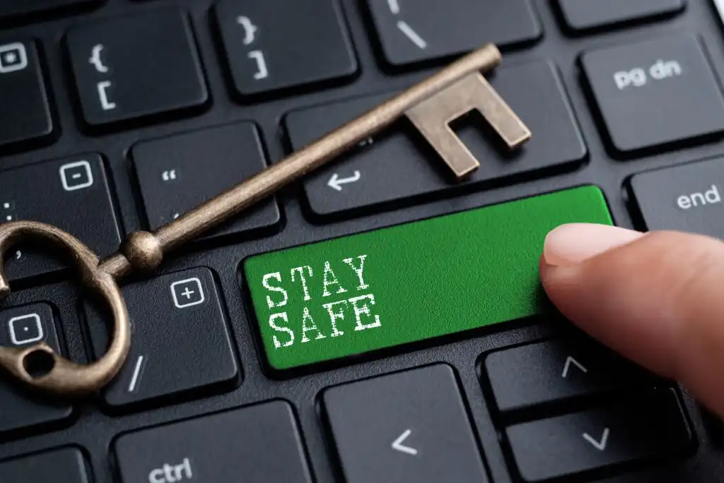 A close-up of a keyboard with a large green key labeled STAY SAFE, next to an old-fashioned key. A persons finger is about to press the green key.