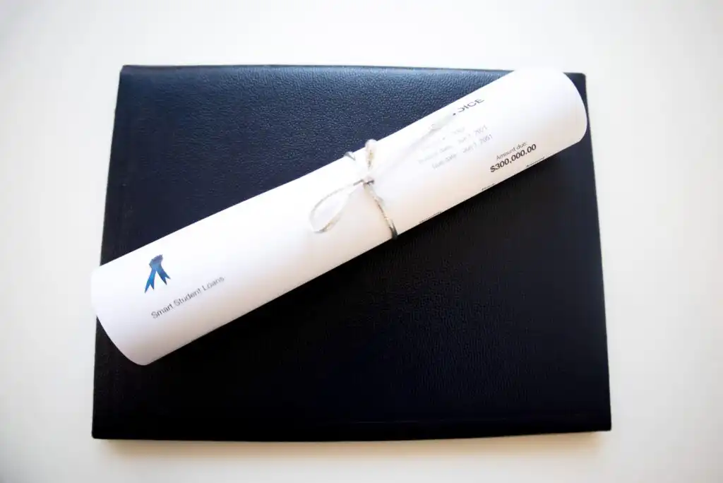 A rolled-up diploma tied with a white string rests on top of a closed black leather folder against a white background.