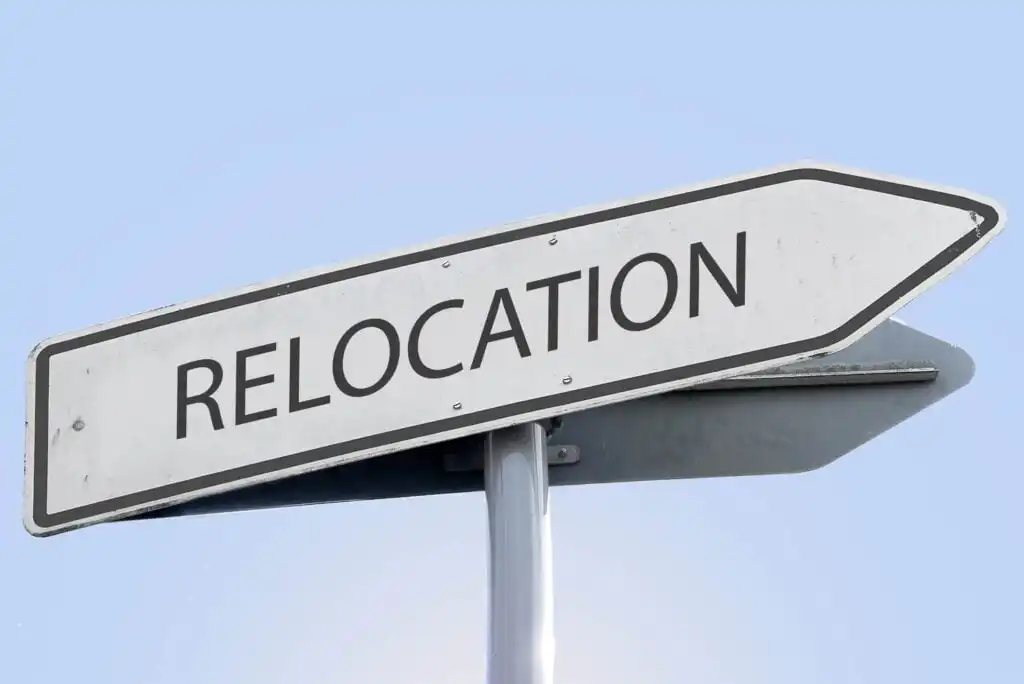 A white road sign with the word RELOCATION in bold black letters points to the right against a clear blue sky.