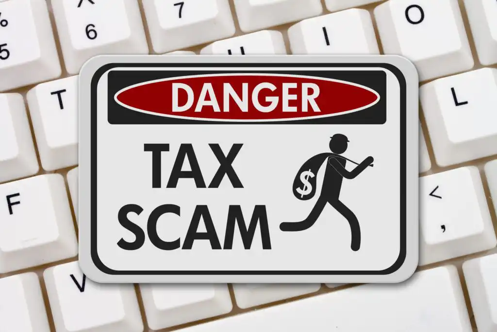 A Danger: Tax Scam warning sign with an icon of a thief carrying a money sack, placed on a white computer keyboard.