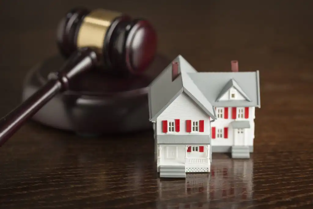 A judges gavel rests on a wooden surface next to a small model house with red shutters and a gray roof, symbolizing legal decisions related to real estate or property law.
