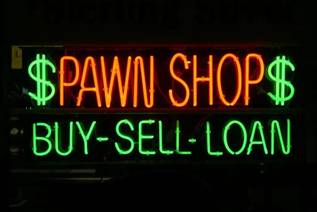 A neon sign displays $ PAWN SHOP $ in red and BUY-SELL-LOAN in green, indicating services offered by the pawn shop.