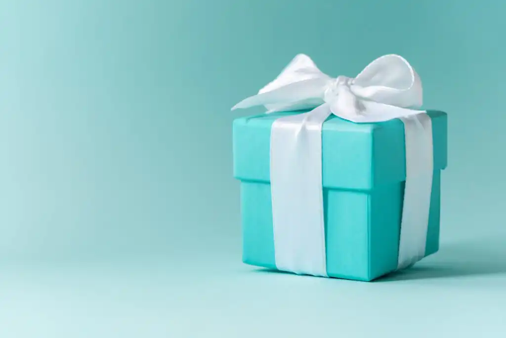 A small turquoise gift box tied with a white satin ribbon bow sits on a matching turquoise background.