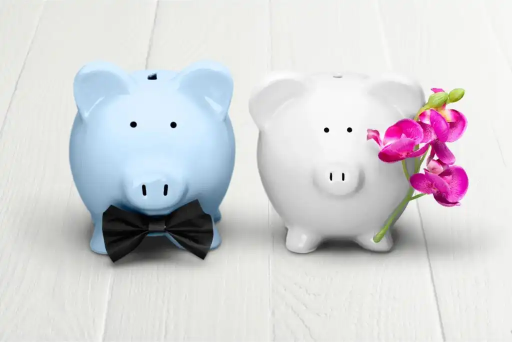 Two piggy banks on a white wooden surface: one blue with a black bow tie, and one white holding a pink orchid flower.
