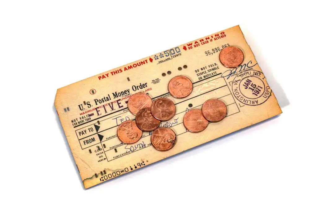 A vintage U.S. Postal Money Order for five dollars, dated 1947, is laid flat with eight pennies scattered on top of it. The money order appears yellowed and slightly worn with age.